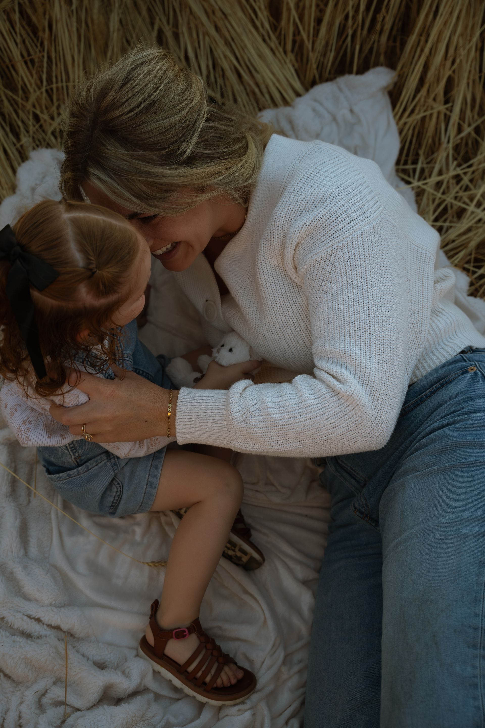 A woman and a little girl are laying on a blanket in a field.