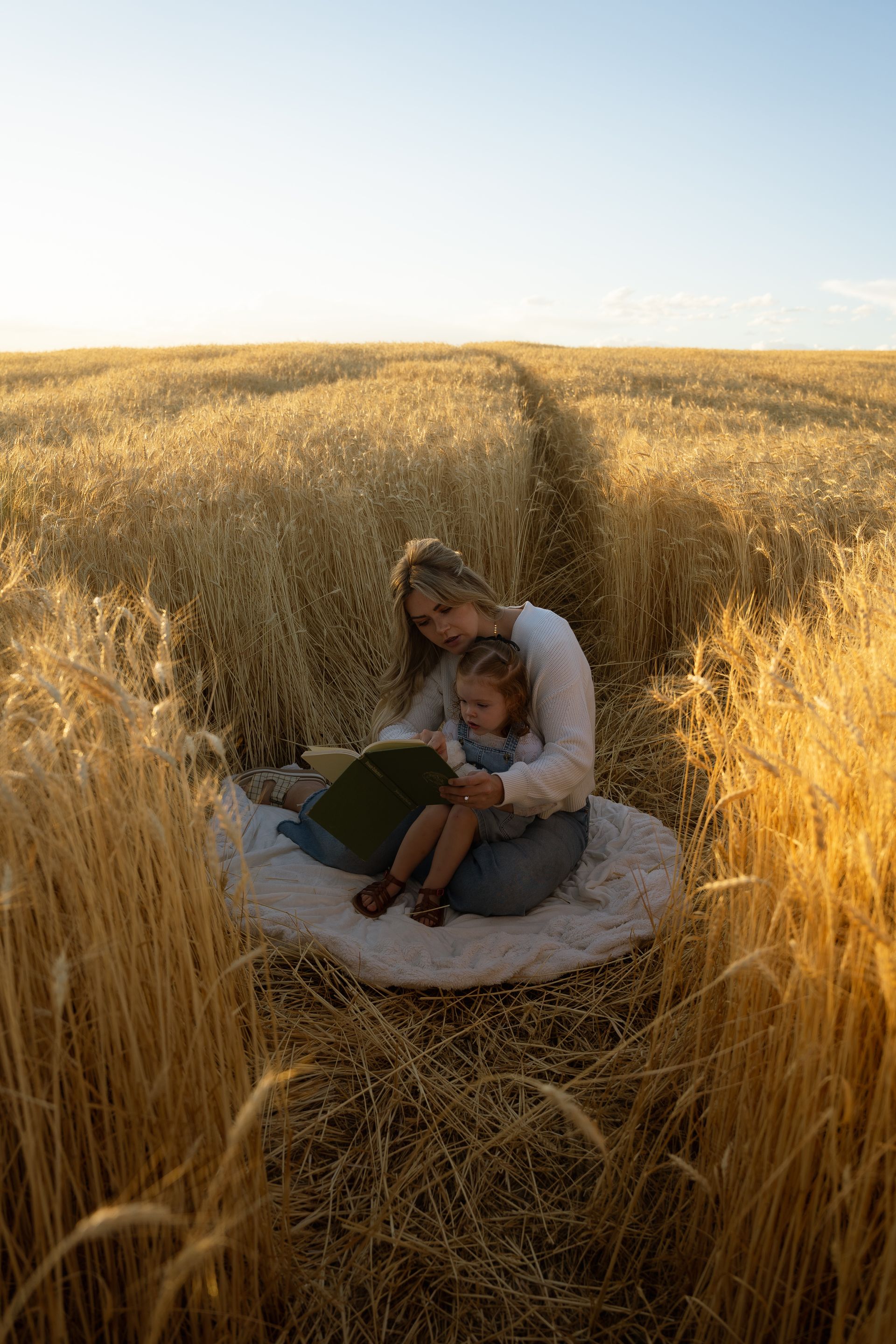 A woman and child are sitting in a field of wheat reading a book.