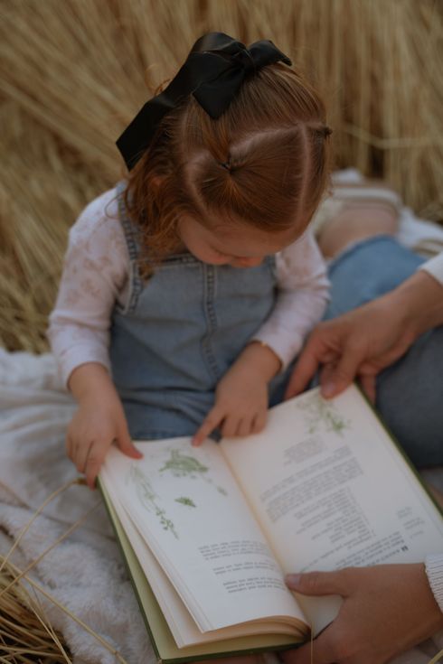 A little girl is sitting on a blanket reading a book.