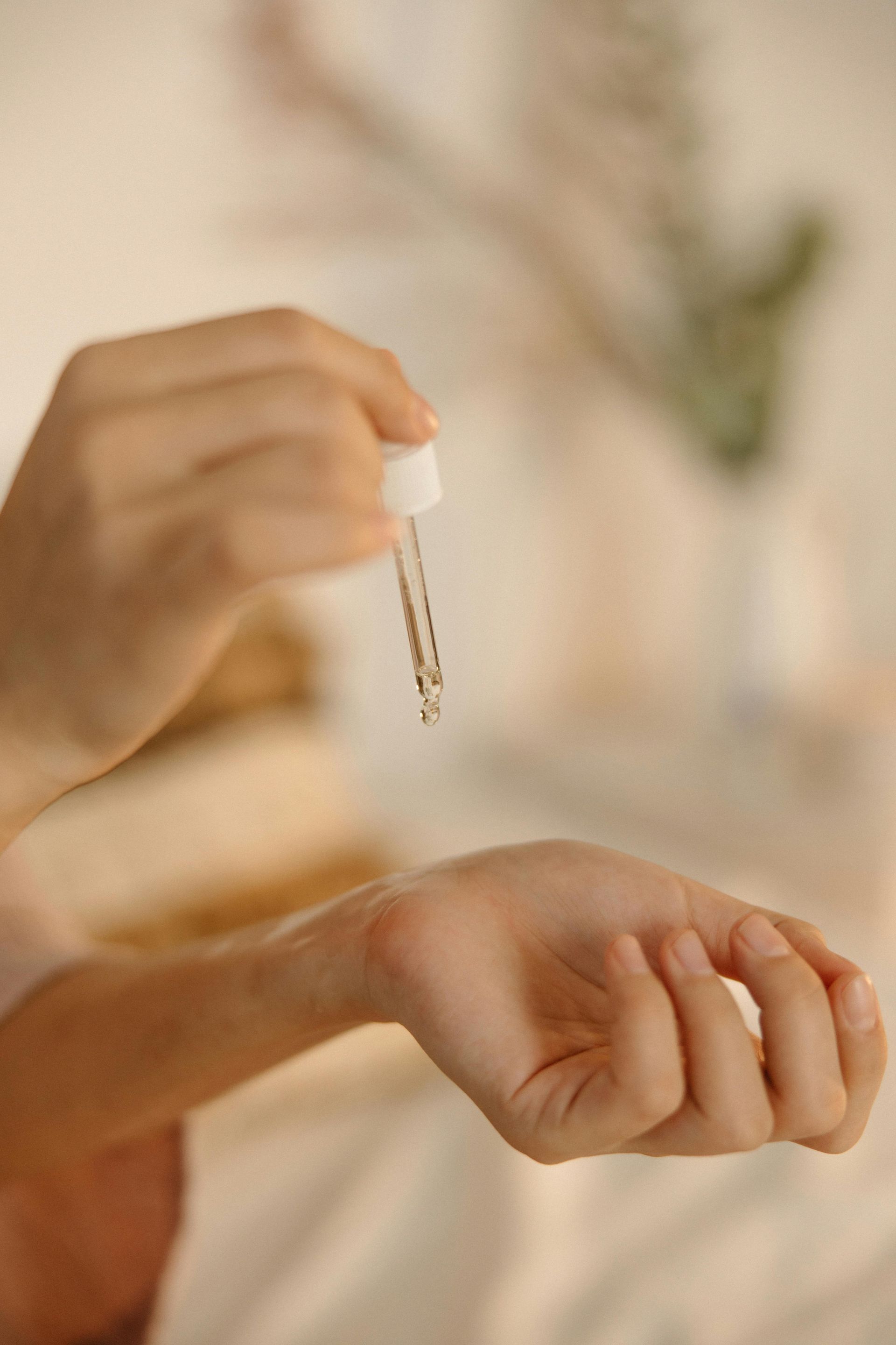 Person holding a dropper dispensing clear liquid onto their wrist indoors.