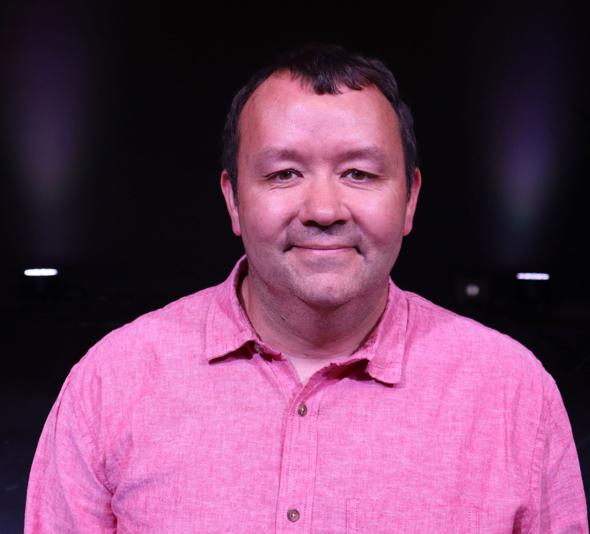 A man in a pink shirt is smiling for the camera.