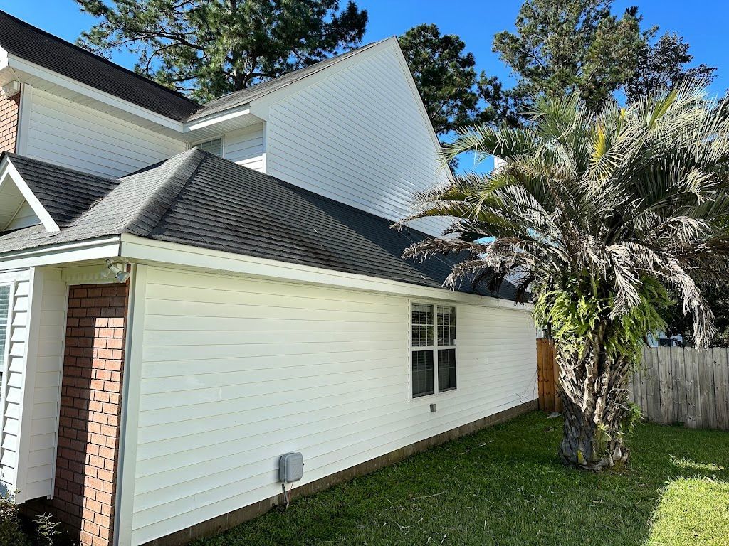 A white house with a black roof and a tree in front of it.