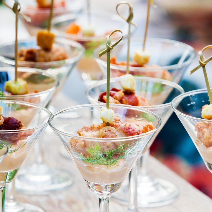 Appetizers in martini glasses with skewers, arranged on a surface.