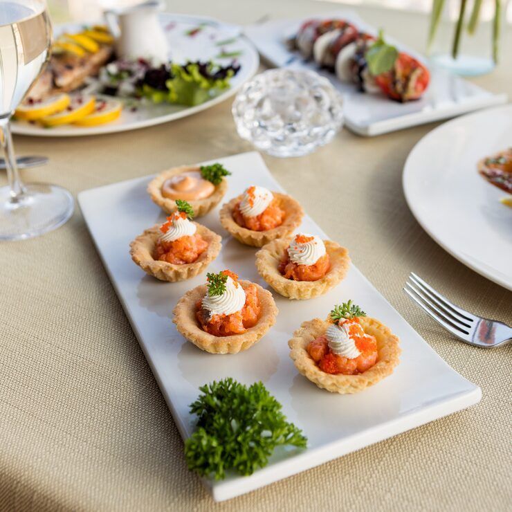 Salmon tartlets on a white platter, part of a table setting with other dishes and a glass of wine.