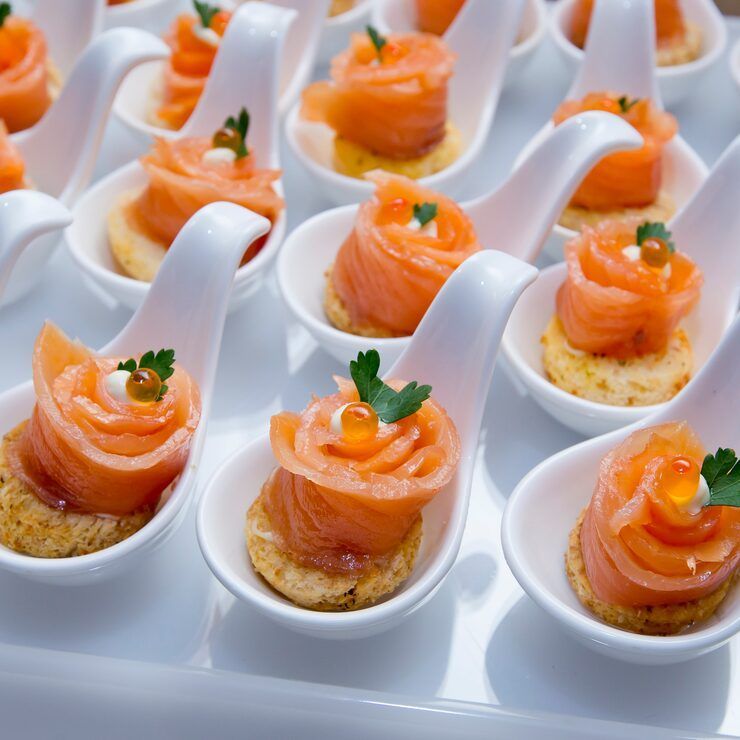 Smoked salmon appetizers on white spoons, garnished with roe and parsley.