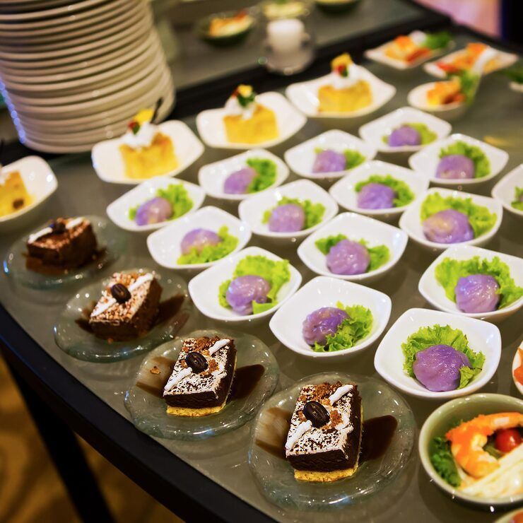 Catering display: Various desserts, including cake, purple balls, and appetizers on a glass table.
