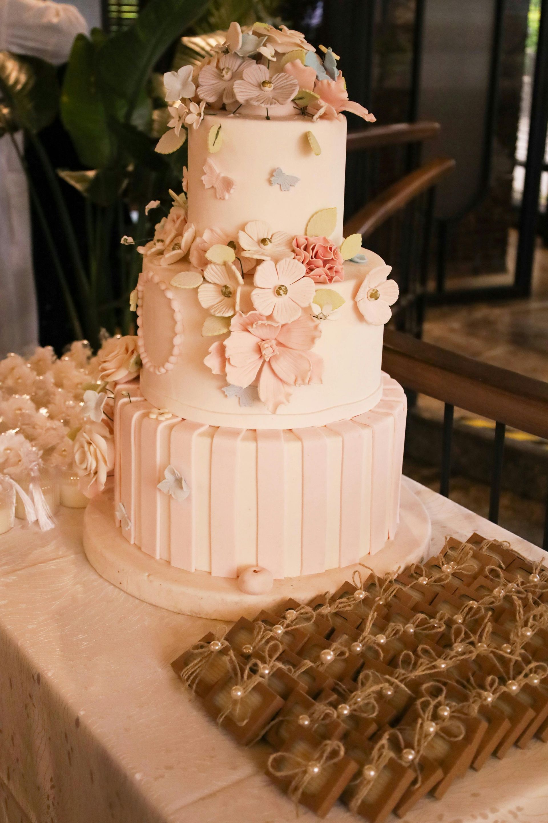 Three-tiered wedding cake decorated with flowers and butterflies. It sits on a table with party favors.