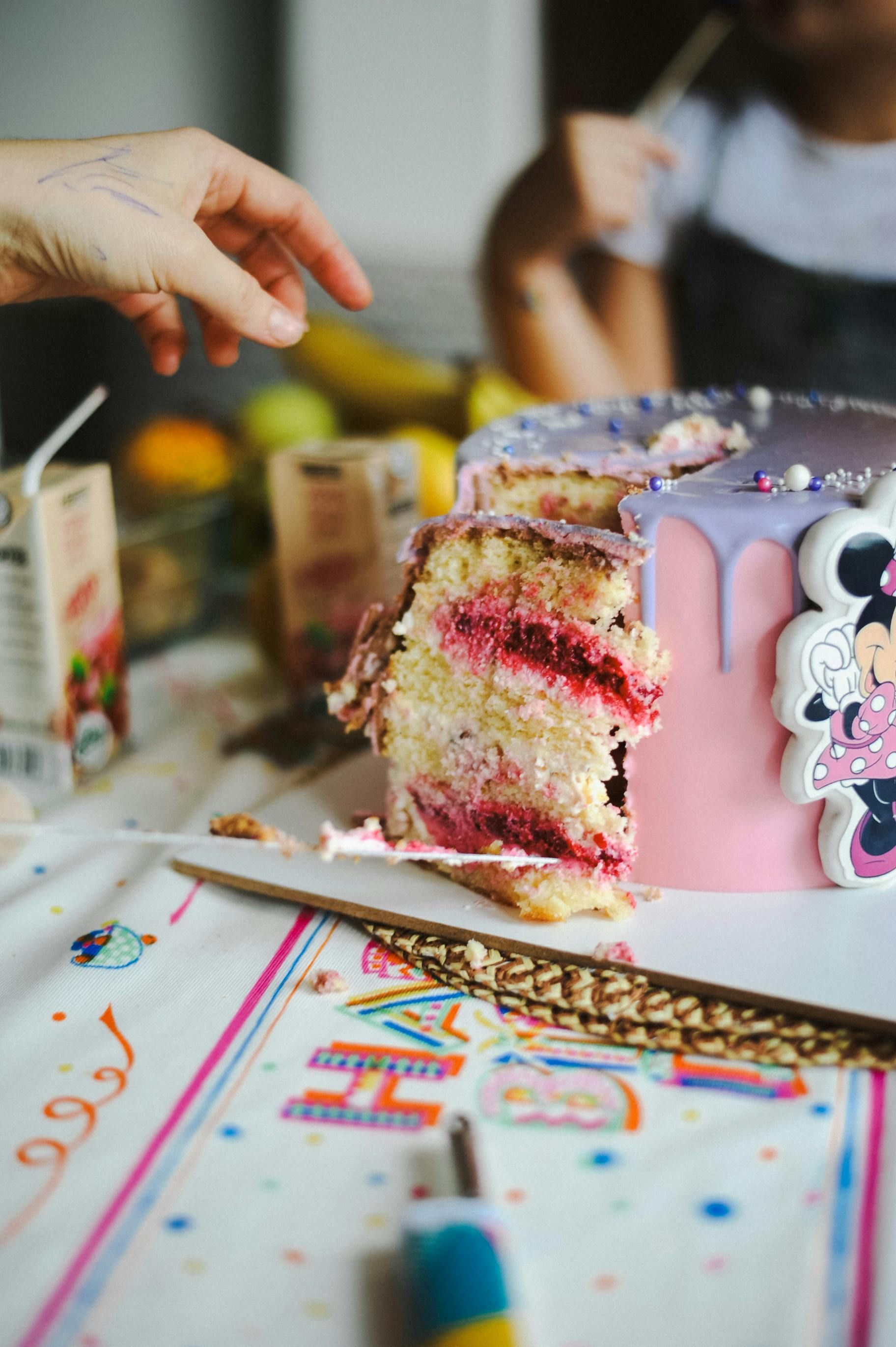 Birthday cake with sparkler, sprinkles, lollipops, and pink candles on a table in front of a pink curtain.