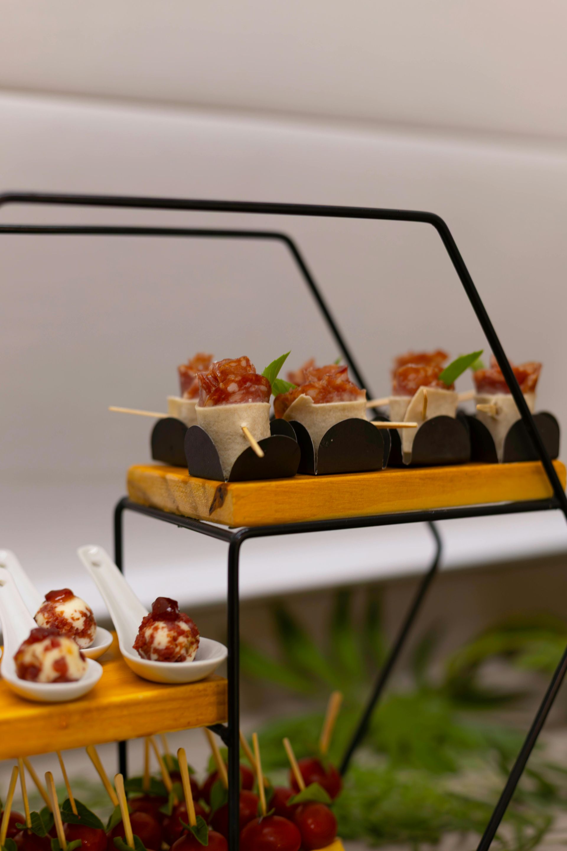 Appetizers on tiered black metal stand. Includes skewers of red grapes and cheese-topped canapés.