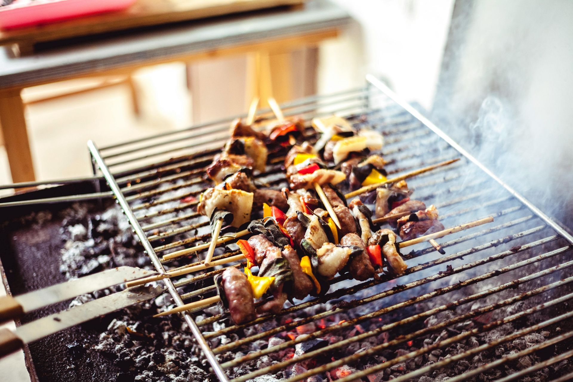 Grilled meat on a metal grate with smoke rising. Someone holds it with wooden chopsticks.
