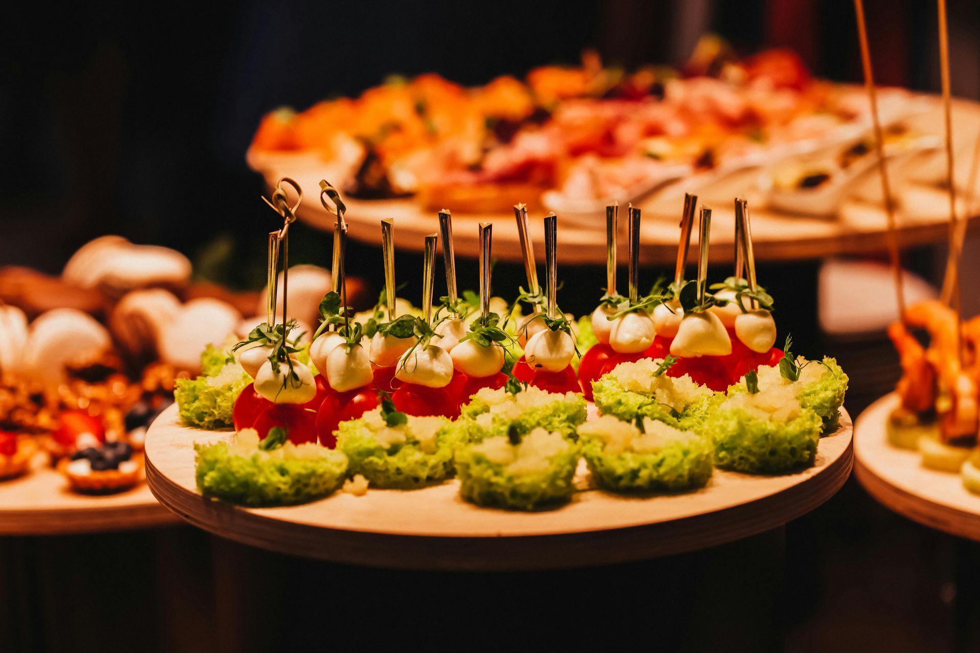 Appetizers on wooden platters: tomatoes topped with mozzarella, lettuce, and other options.
