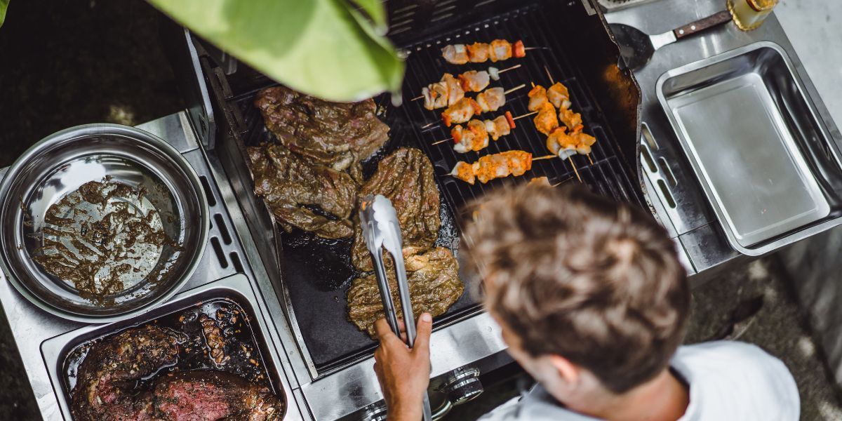 Grilled pork skewers on a wooden board with rosemary, lemon, and spice jar.