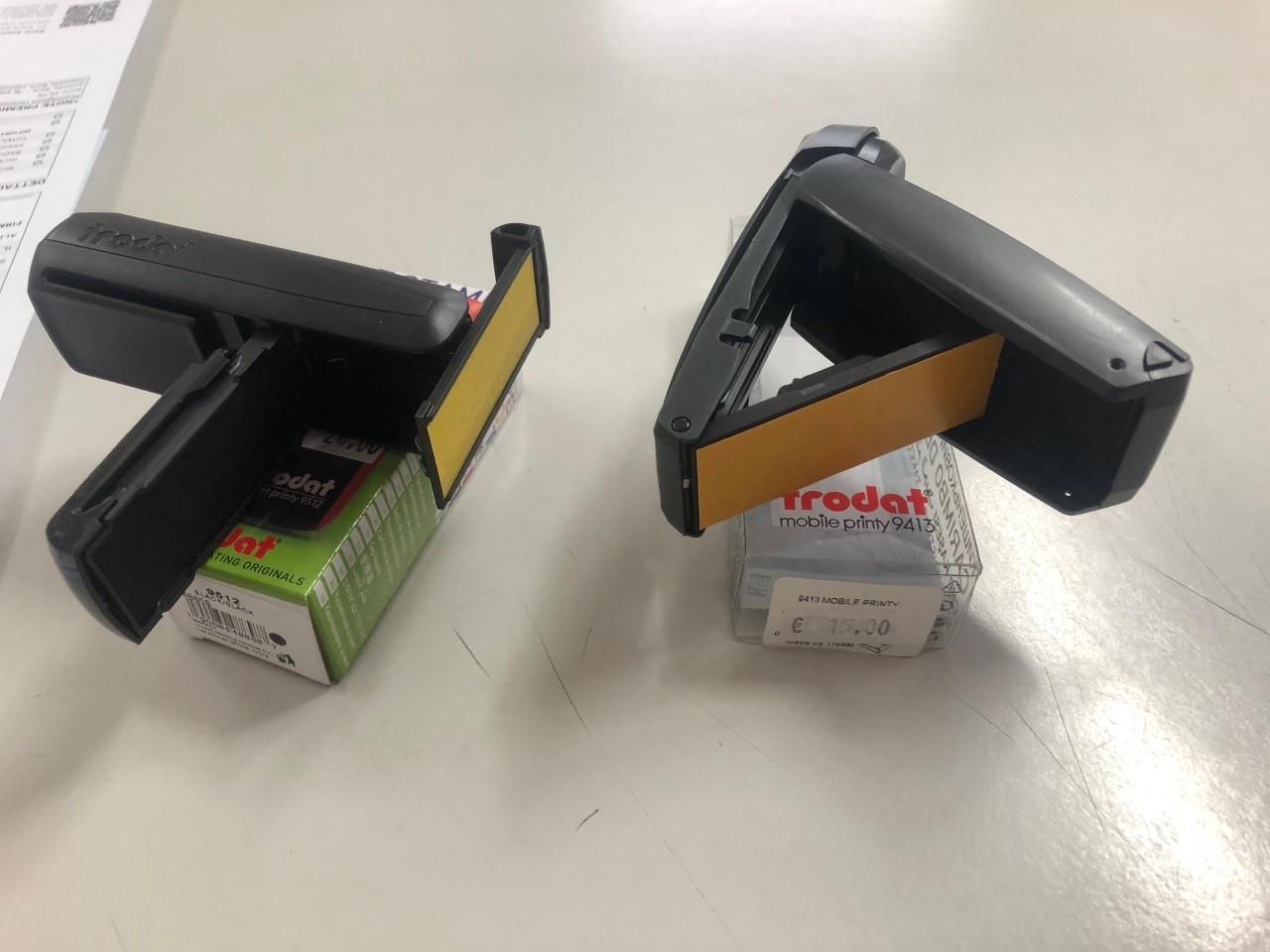 Due timbri neri con tamponi di inchiostro giallo, appoggiati su pile di piccole scatole verdi e bianche su un tavolo.