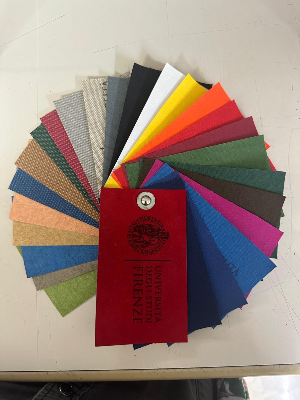 La collezione di campioni si è aperta a ventaglio, mostrando tessuti di vari colori, con il cartellino rosso al centro.