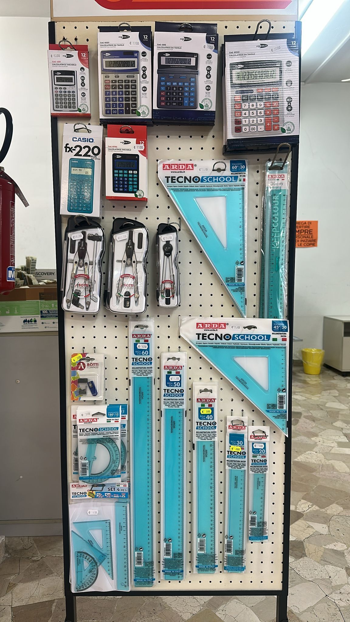 Espositore con vari materiali scolastici: calcolatrici, righelli e goniometri.