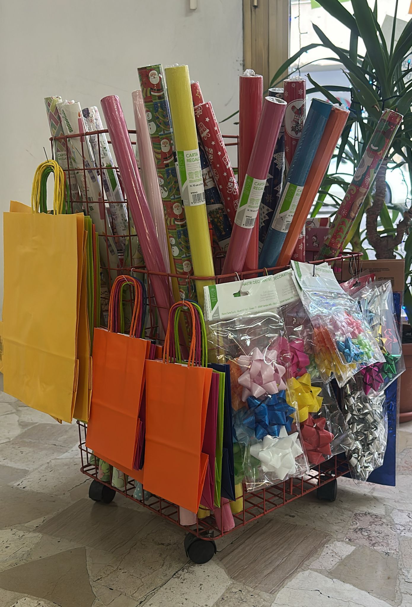 Un carrello pieno di materiale per confezionare i regali: rotoli di carta, sacchetti e fiocchi.