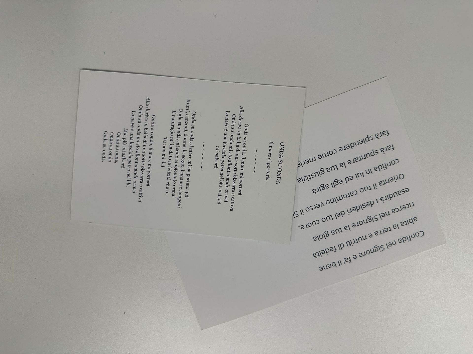 Due fogli bianchi con testo nero su una superficie bianca; i fogli sono leggermente sovrapposti e inclinati.