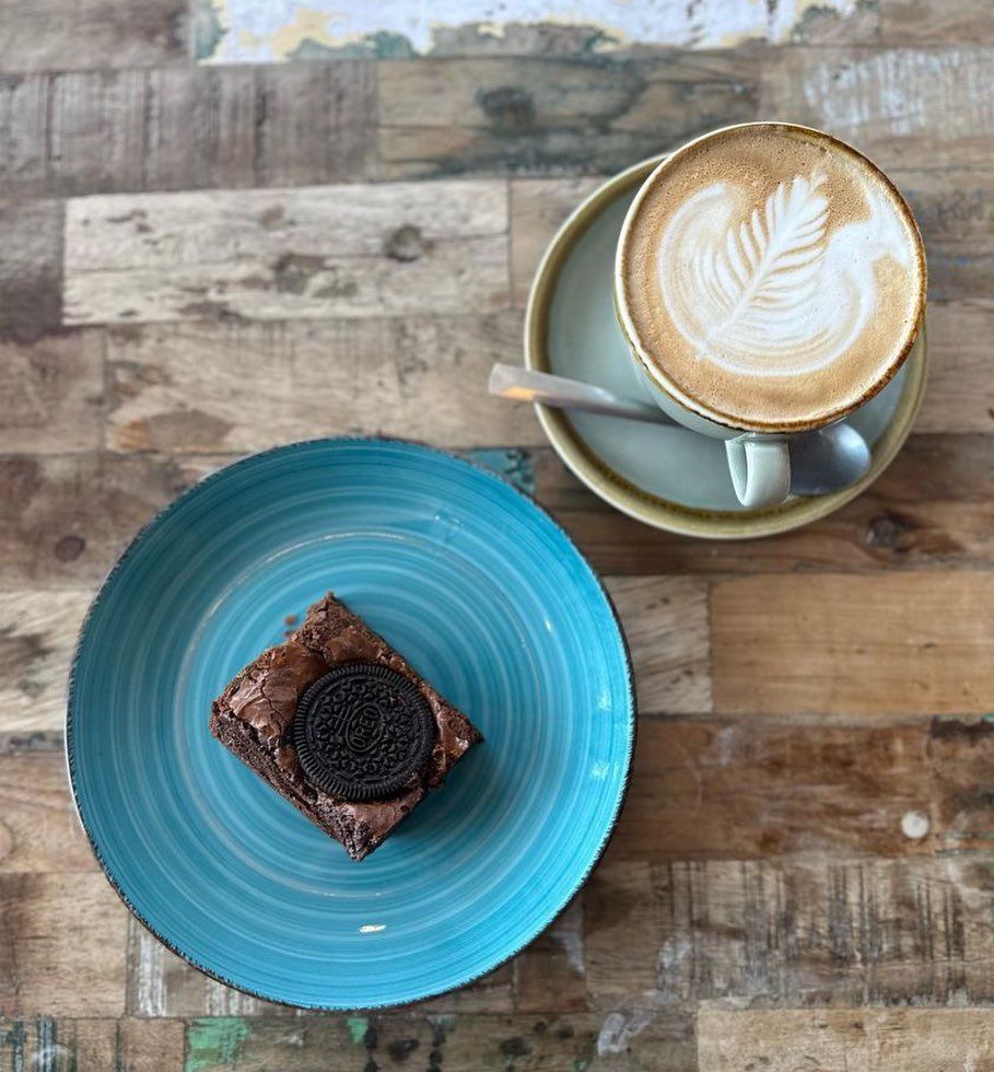 a blue plate with a brownie and a cup of coffee on a wooden table .