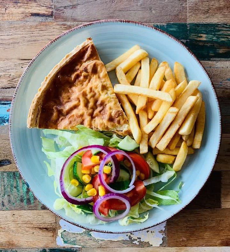 a plate of food with a slice of quiche and french fries on a wooden table .