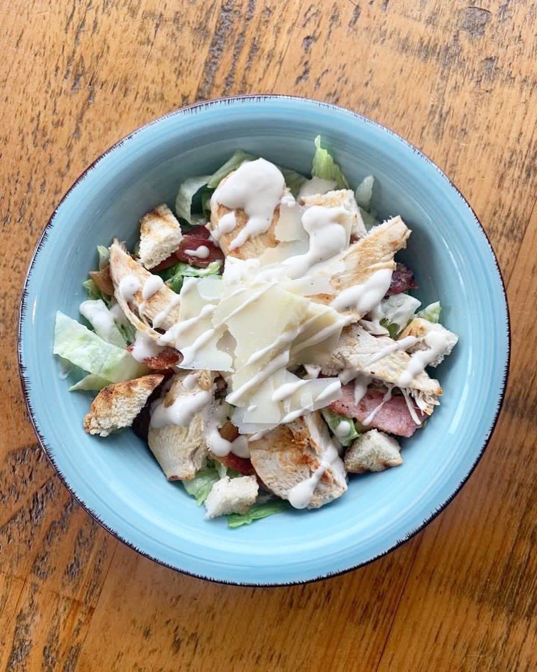 a blue bowl filled with chicken salad on a wooden table .