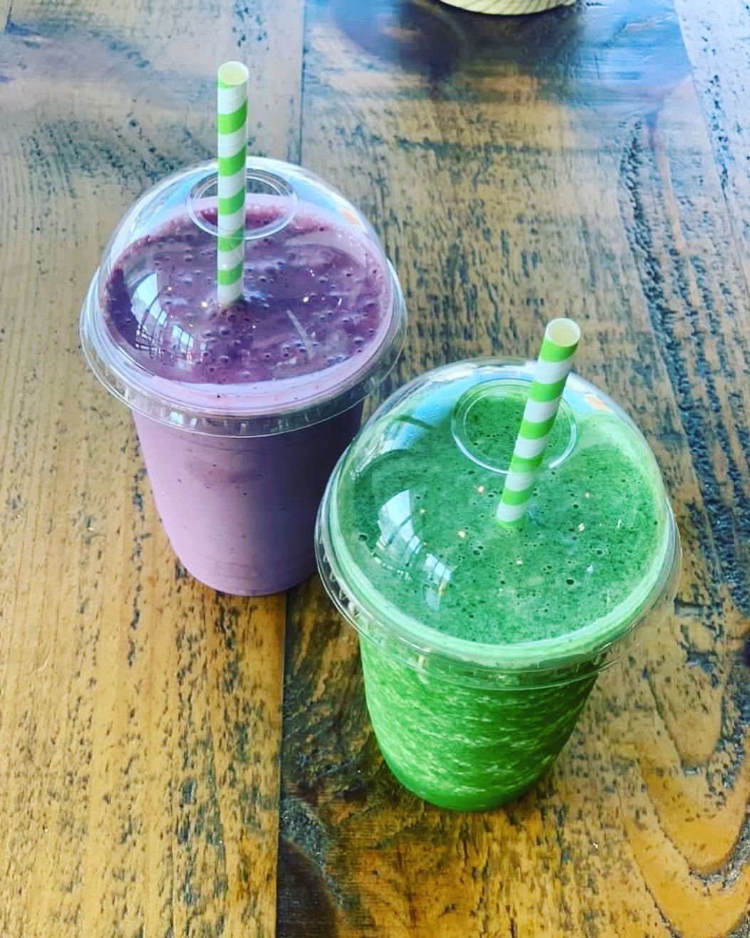 two cups of smoothies with straws on a wooden table .