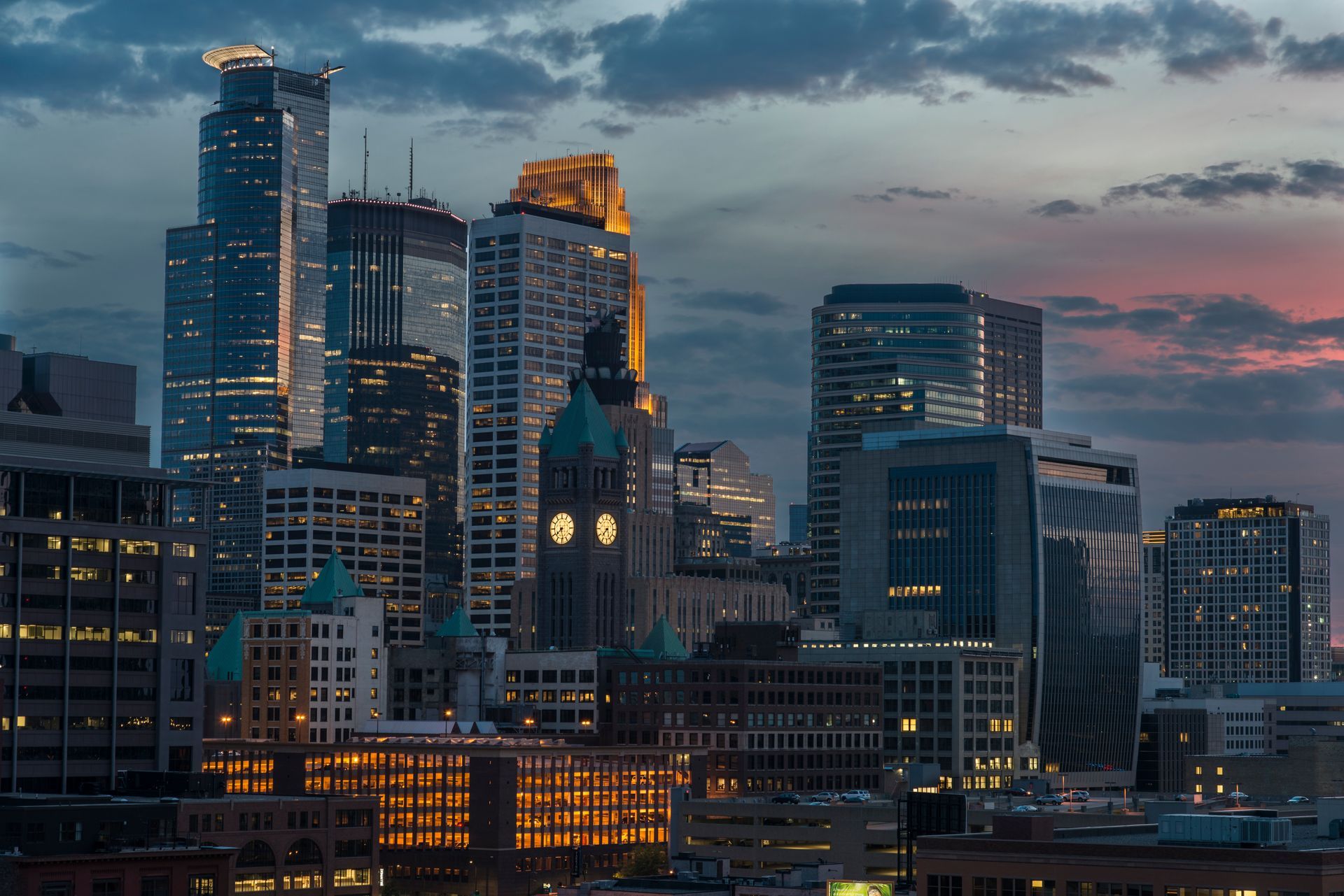 A city skyline at night with a sunset in the background.