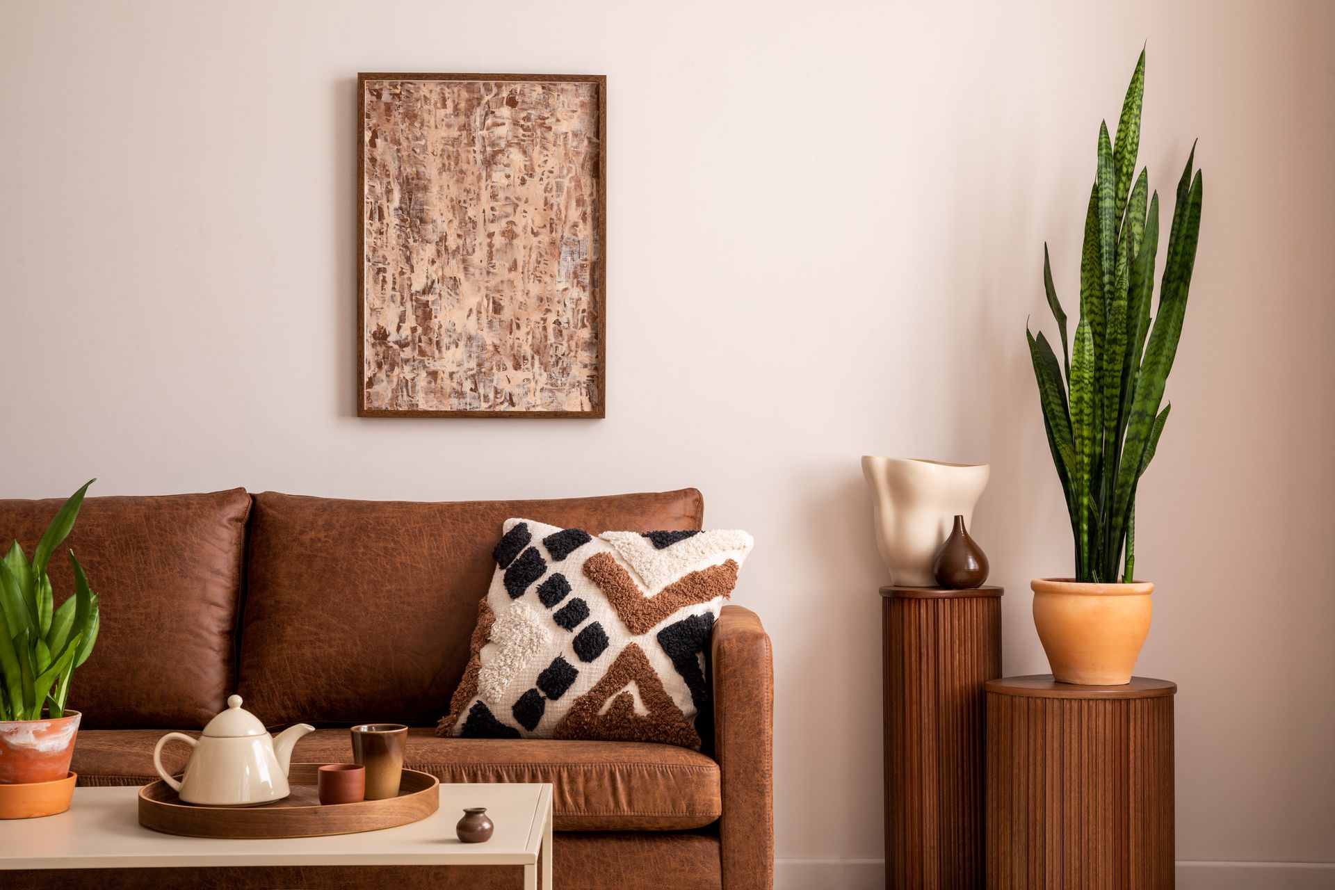 A living room with a brown couch , coffee table , and potted plants.