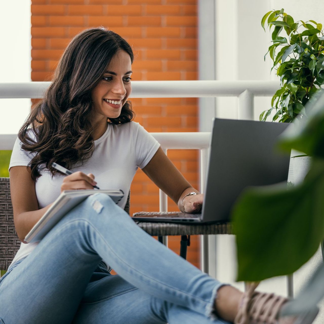 A woman is sitting on a balcony using a laptop computer