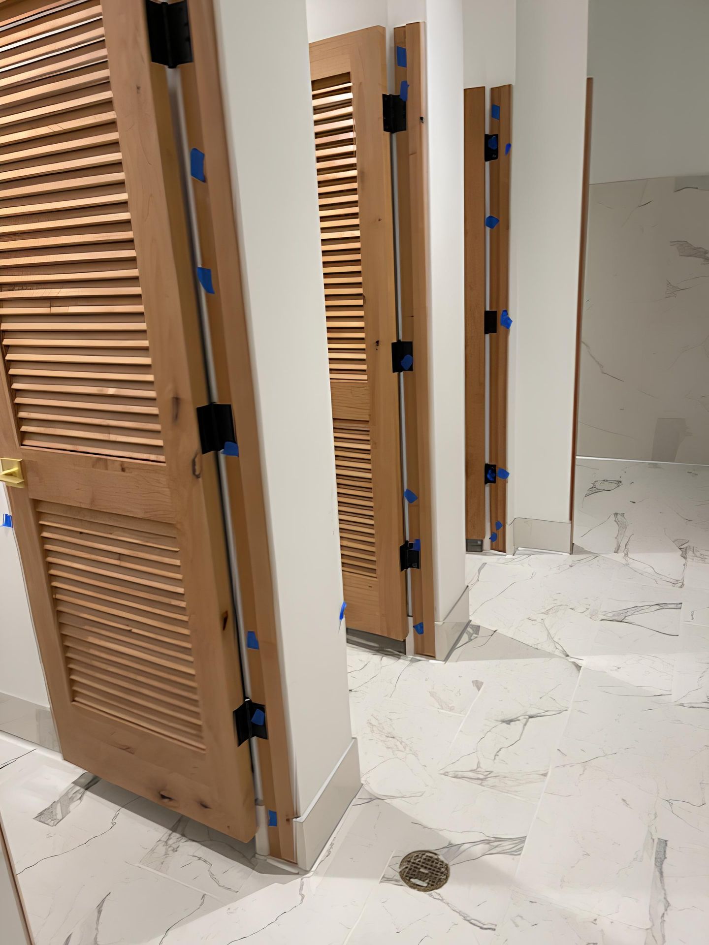 A row of wooden doors in a bathroom with marble floors.