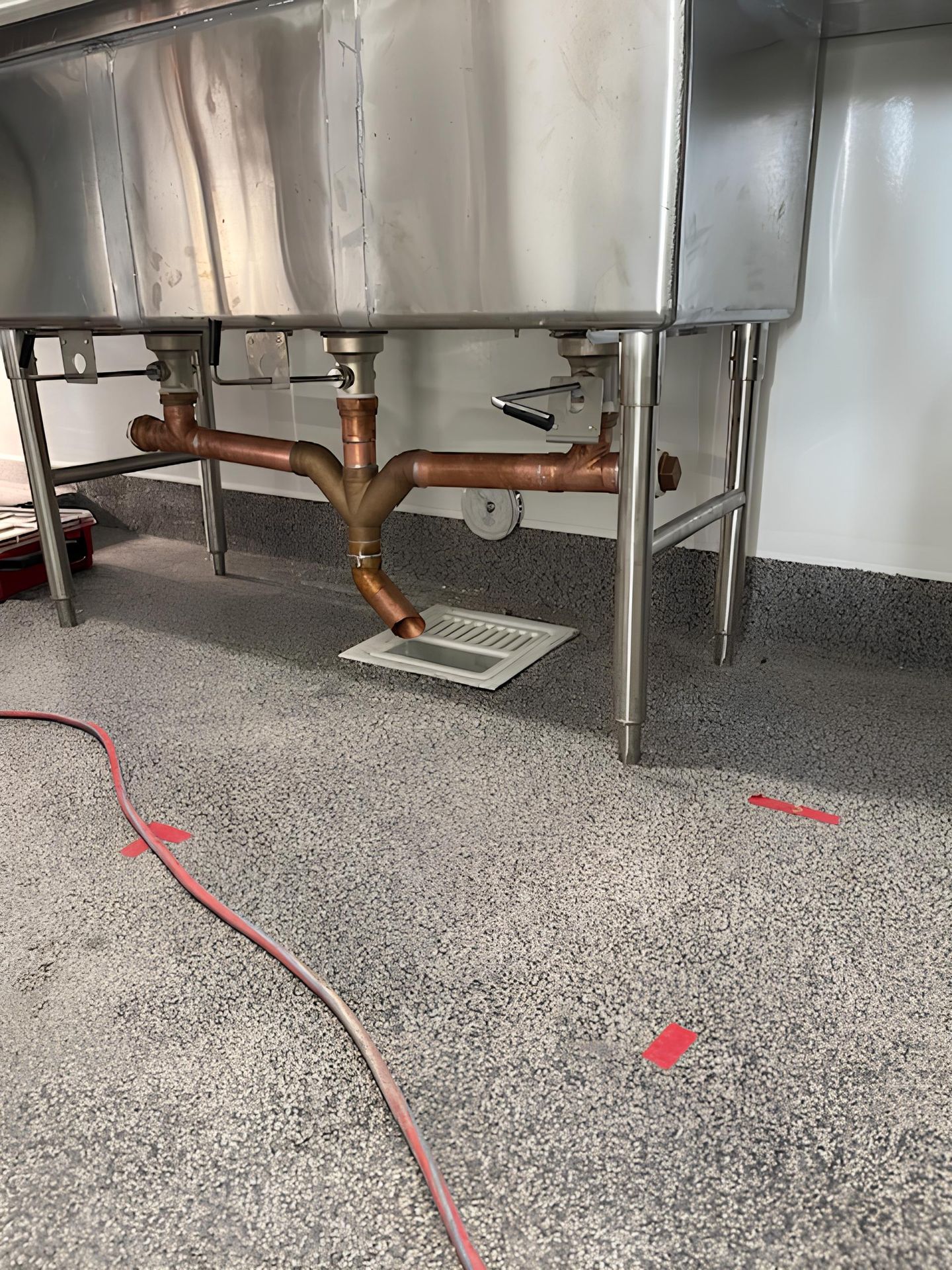 A stainless steel sink with copper pipes underneath it in a kitchen.