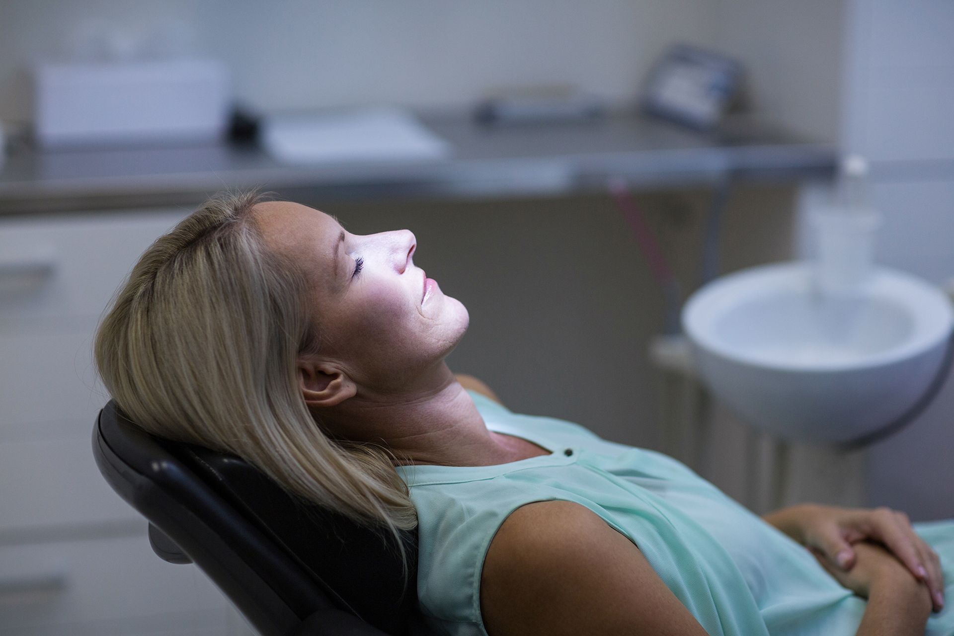 Woman reclined in a dentist chair, looking up at a light.