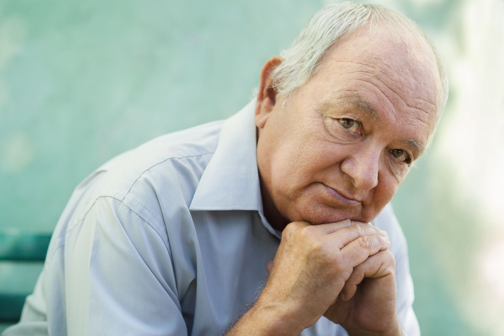 An older man is sitting with his hands on his chin and looking at the camera.