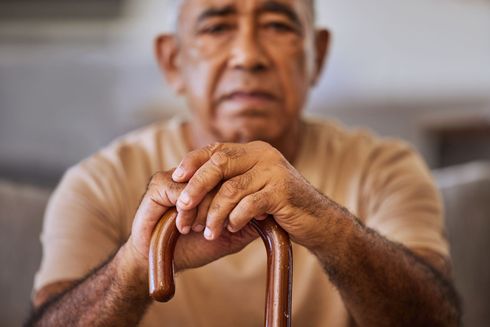 An elderly depressed man is sitting on a couch holding a cane that could use behavioral health integration (BHI) services.