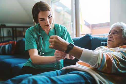 A nurse is checking an elderly woman 's wrist with a smart watch for remote patient monitoring (RPM) services.
