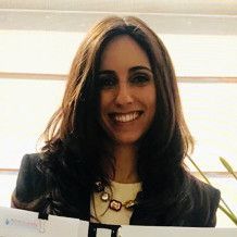 A woman is smiling and holding a piece of paper in front of a window.