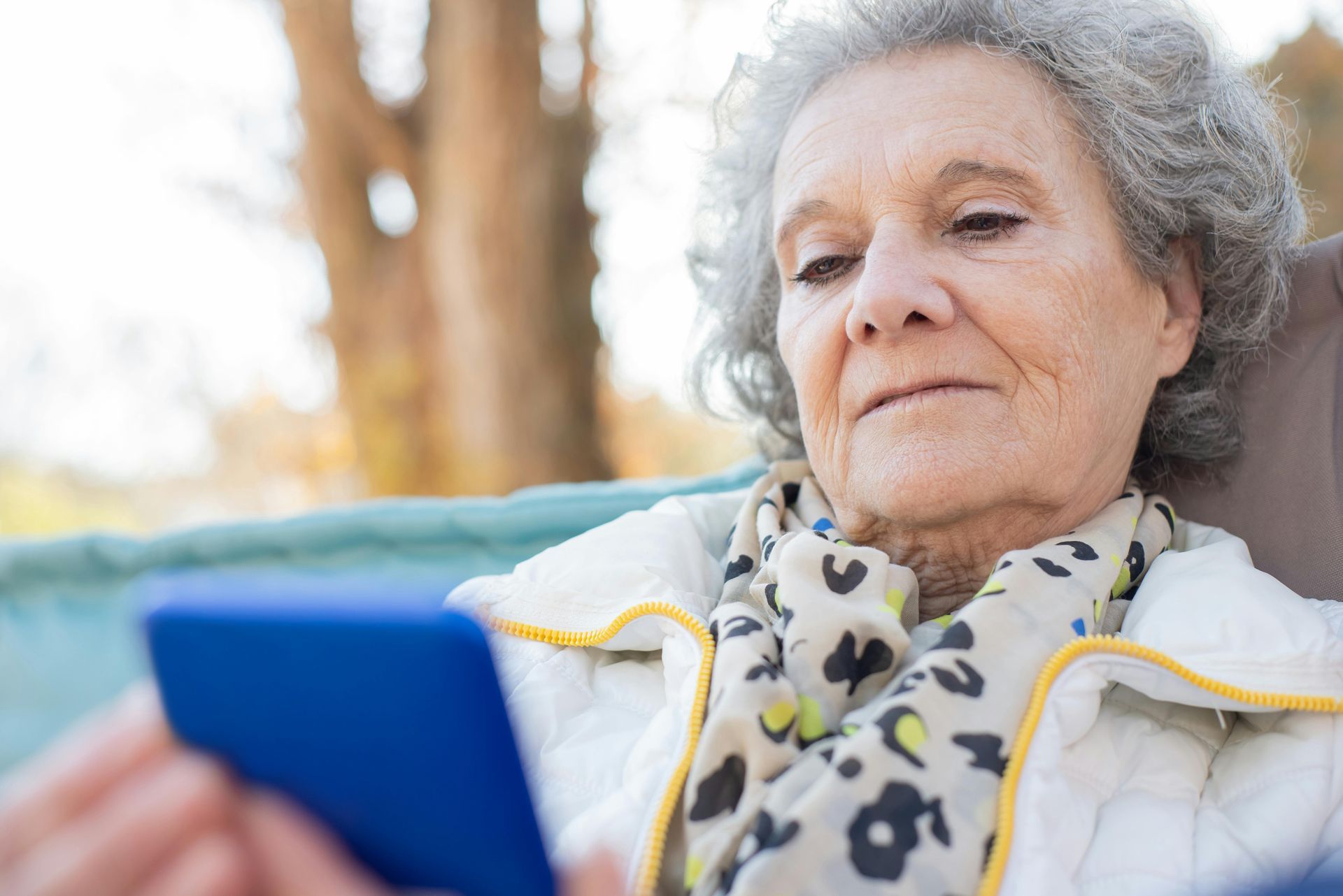 Older female is sitting outdoors while holding a smartphone and reading something important.