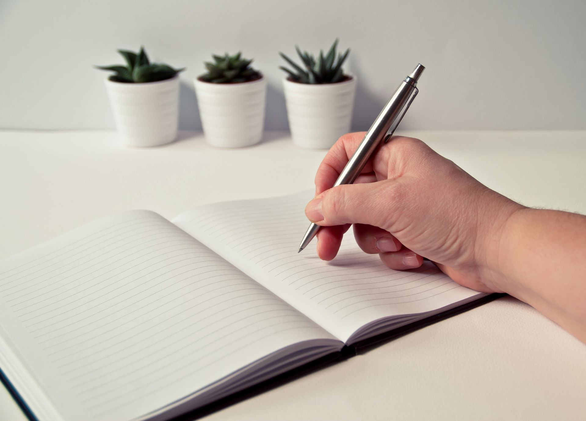 Image that shows a hand with a pen getting ready to document findings in an open notebook.