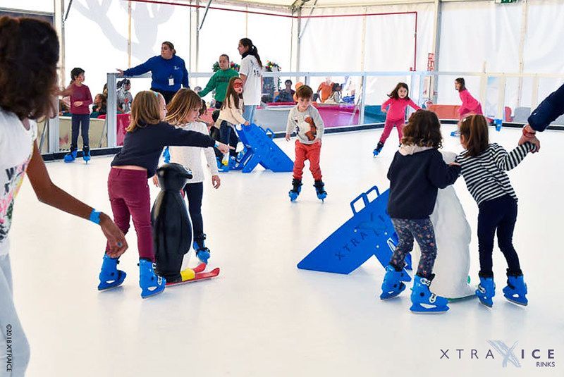 A group of children are ice skating on a rink.