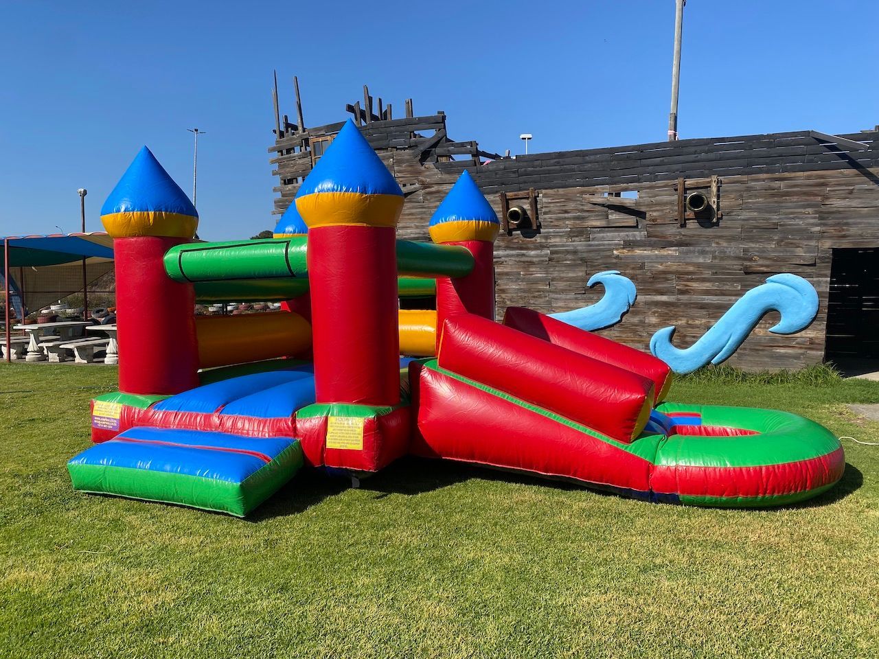 A bouncy castle with a slide is sitting in the grass in front of a wooden building.