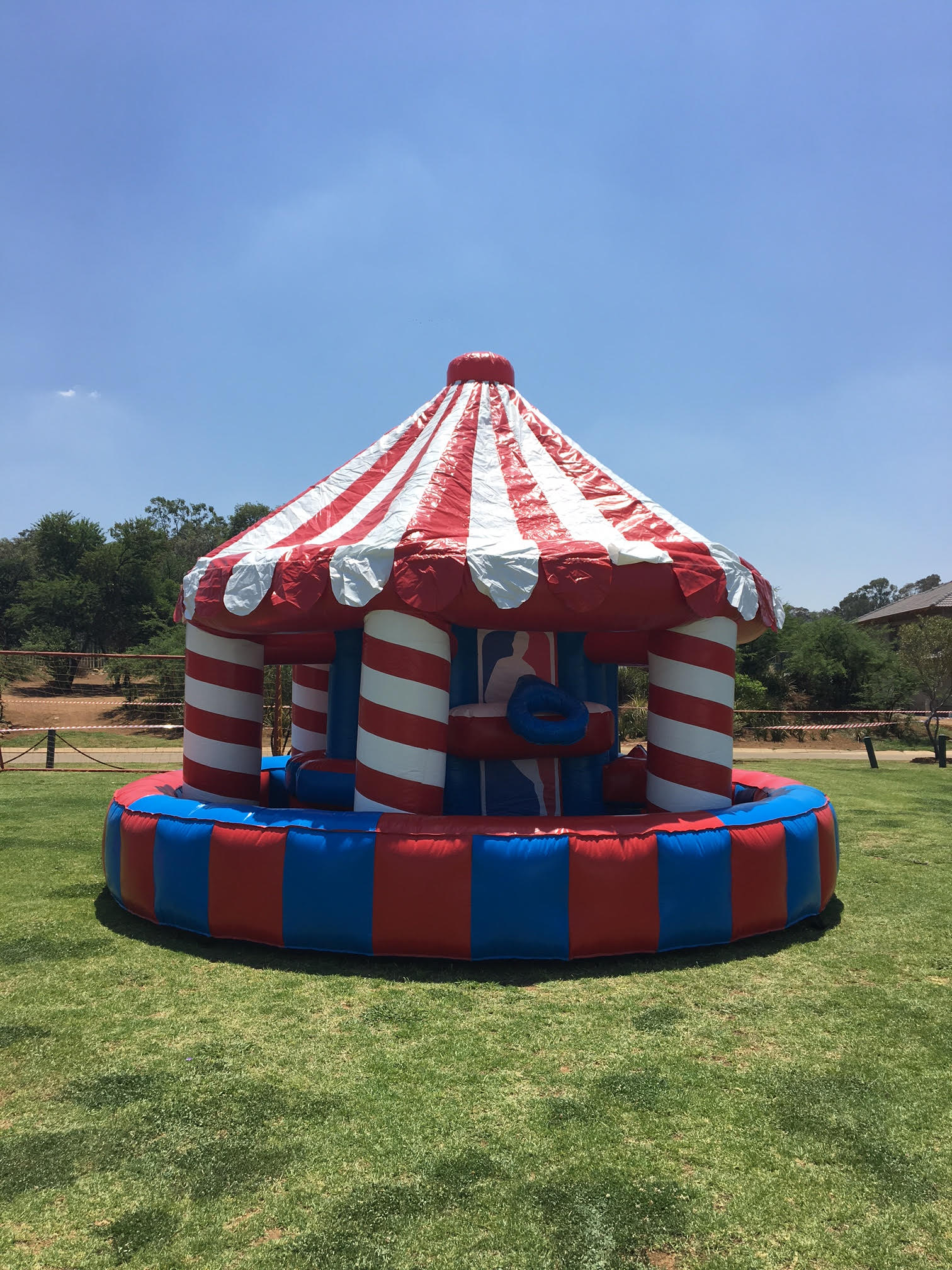 A red , white and blue inflatable merry go round is sitting on top of a lush green field.