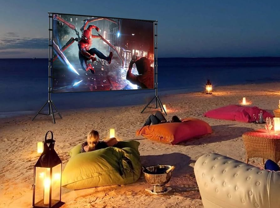 Beachside movie night: Spider-Man film on large screen, people lounging on beanbags, lanterns illuminate the scene.
