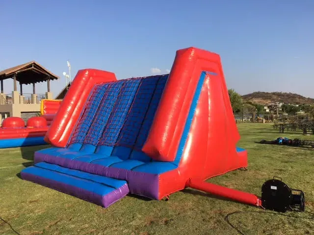 A red and blue inflatable slide is sitting on top of a lush green field.