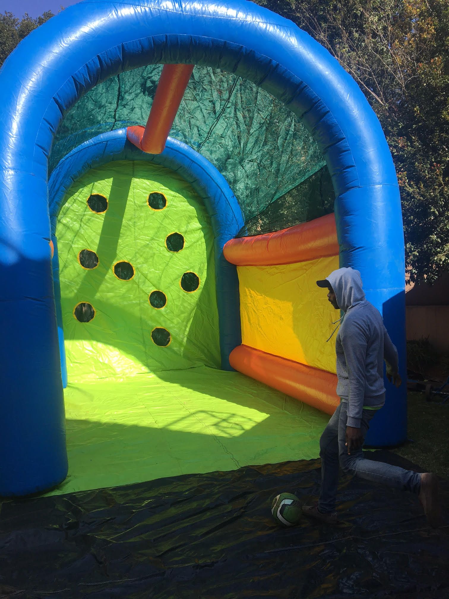 A man is kicking a soccer ball in front of a bouncy house.