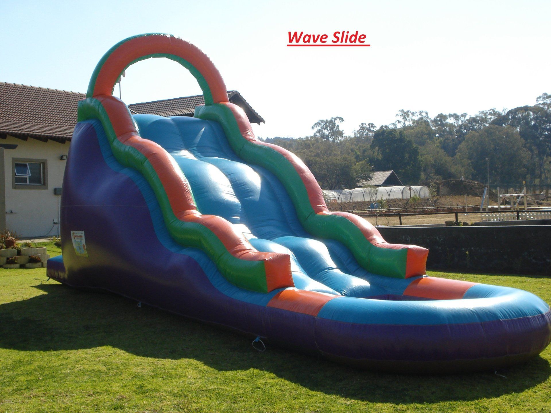 An inflatable wave slide is sitting in the grass in front of a house
