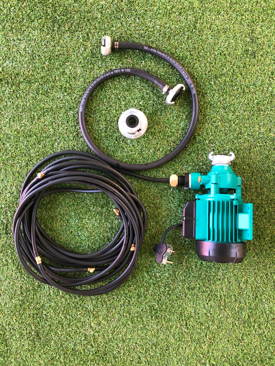 A green water pump with a hose attached to it is sitting on top of a lush green field.