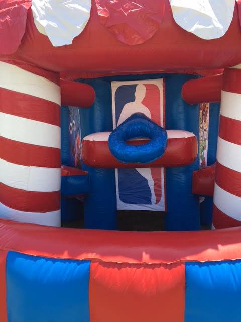 A red white and blue bouncy house with a basketball hoop