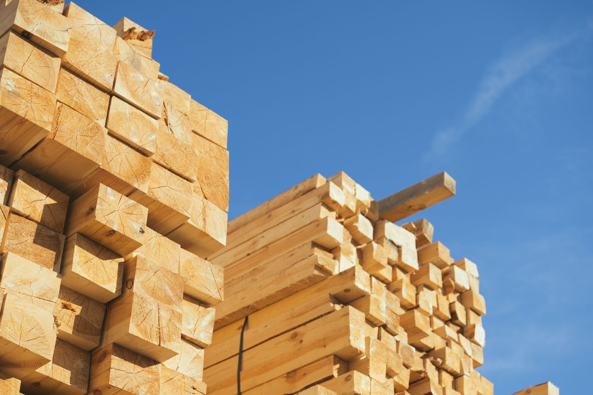 Stacks of cut lumber piled outdoors under a clear blue sky.