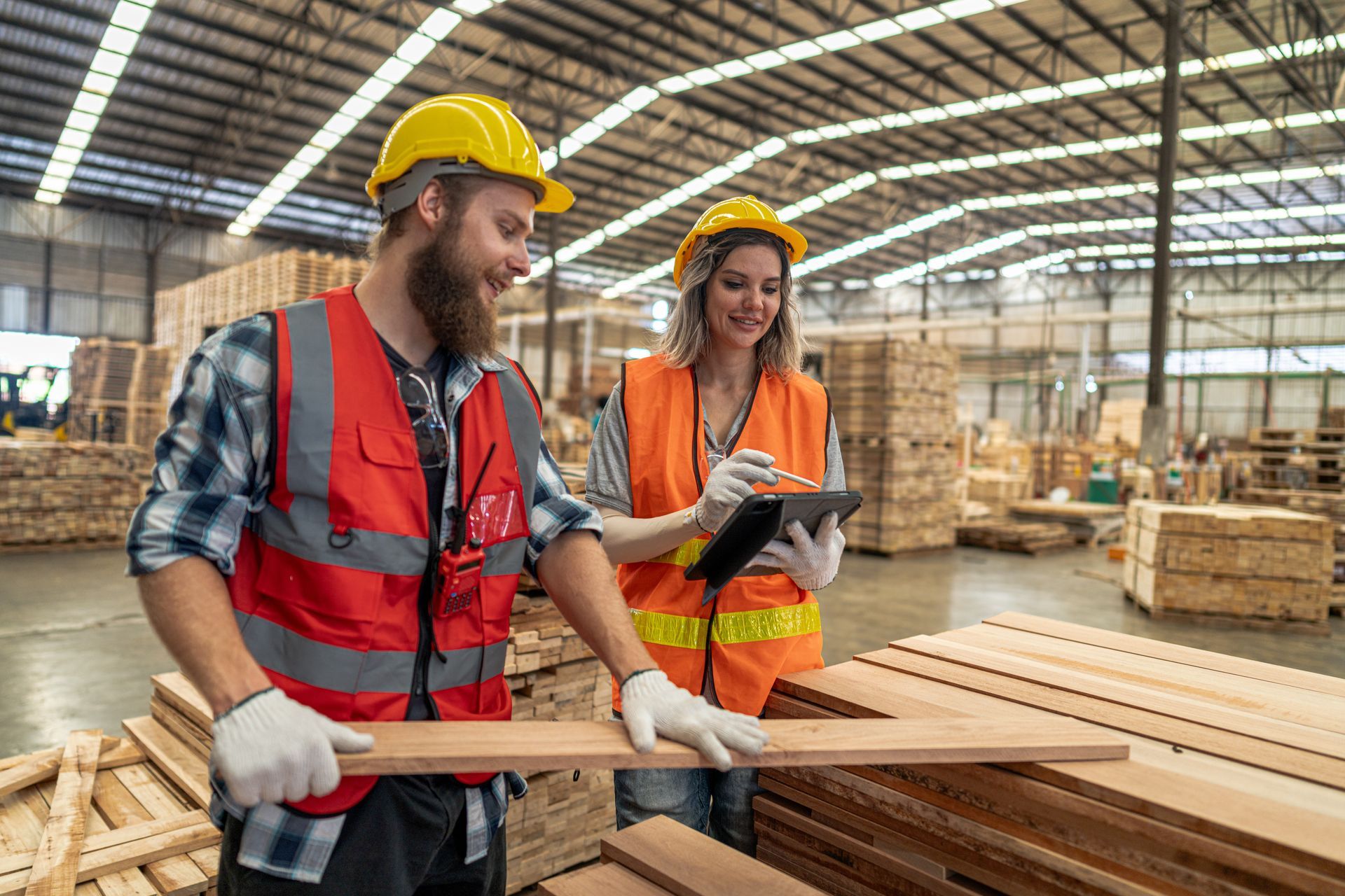 Two workers wearing safety gear working by wooden products at a warehouse. Two workers wearing safety gear working by wooden products at a warehouse.