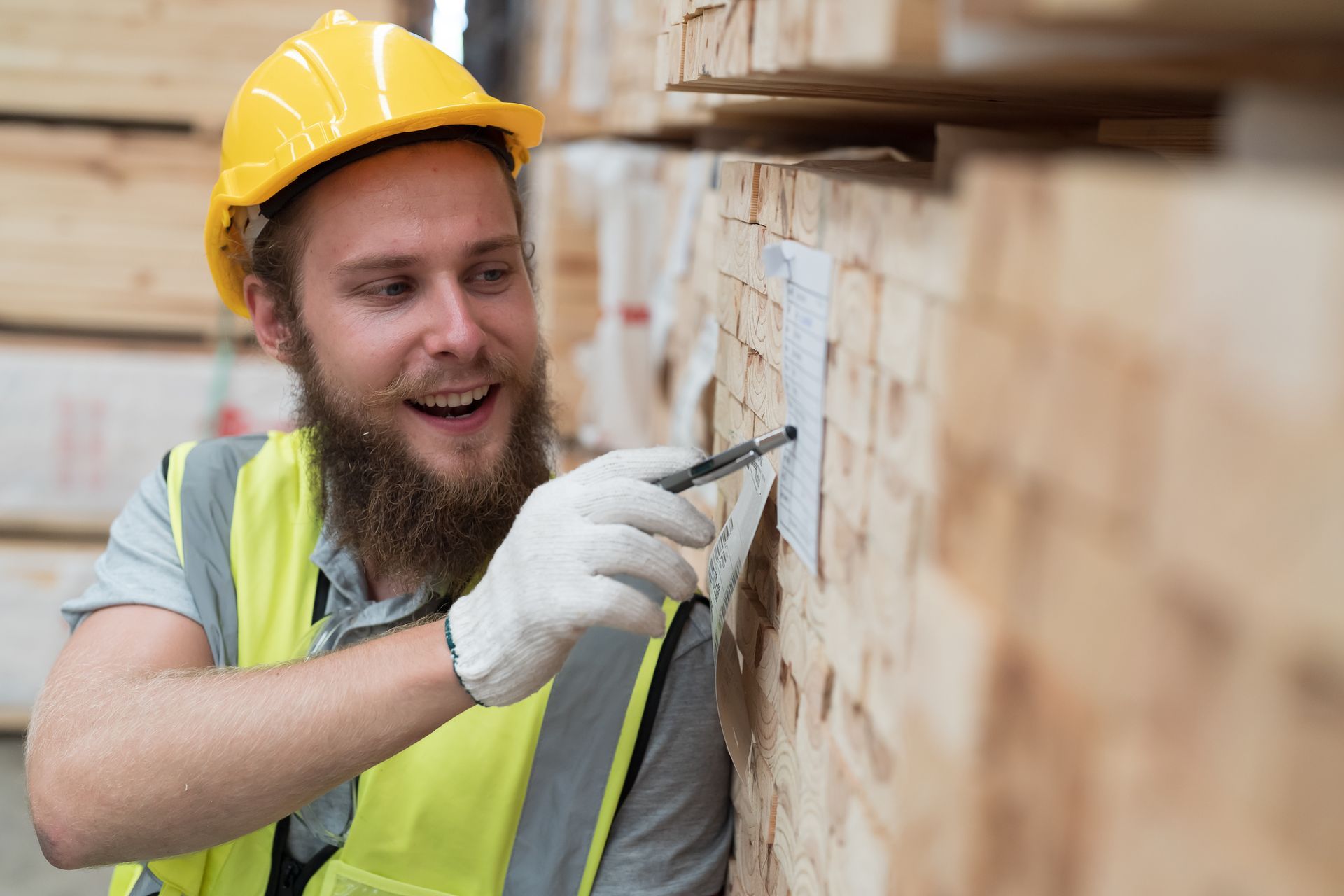 A warehouse worker pointing at a note with a pen on piles of timber products.