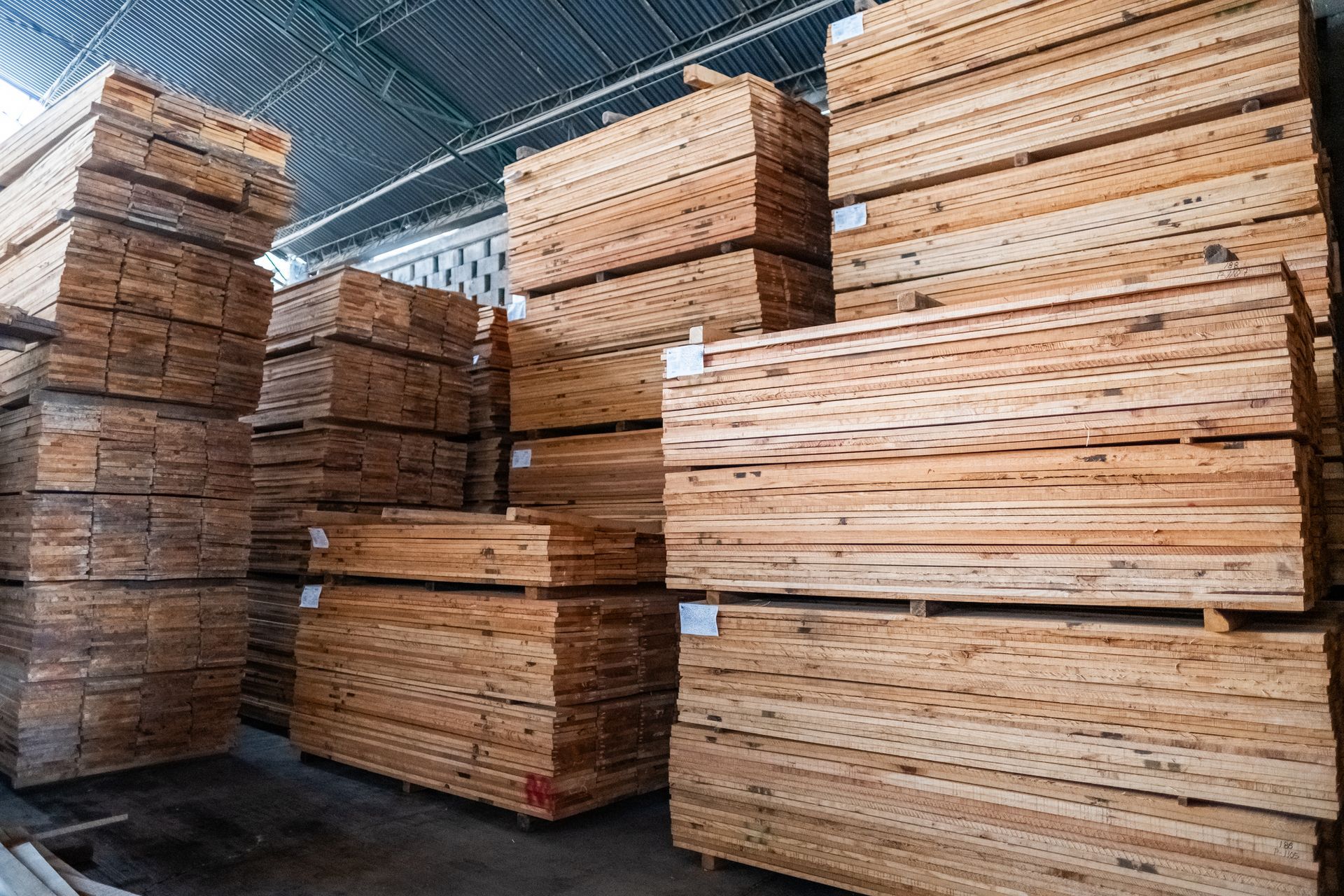 Stacks of wooden planks in a warehouse with metal roof and brick walls